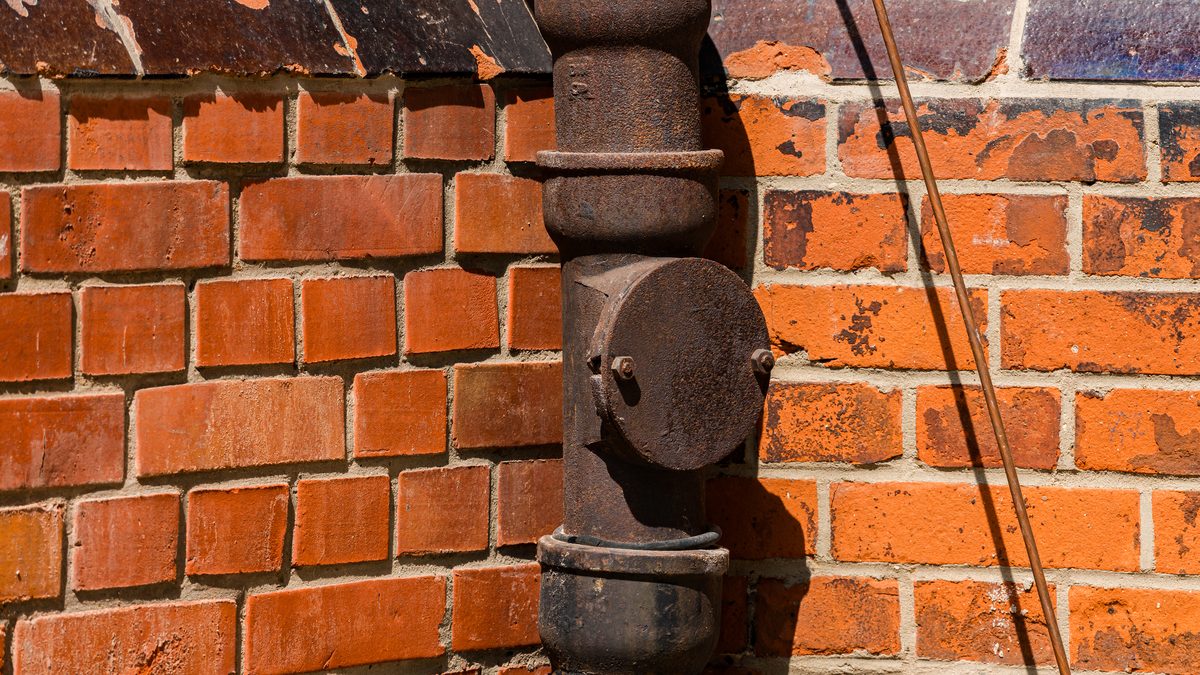 Cast iron soil stack with a bolted access cover on a brick wall