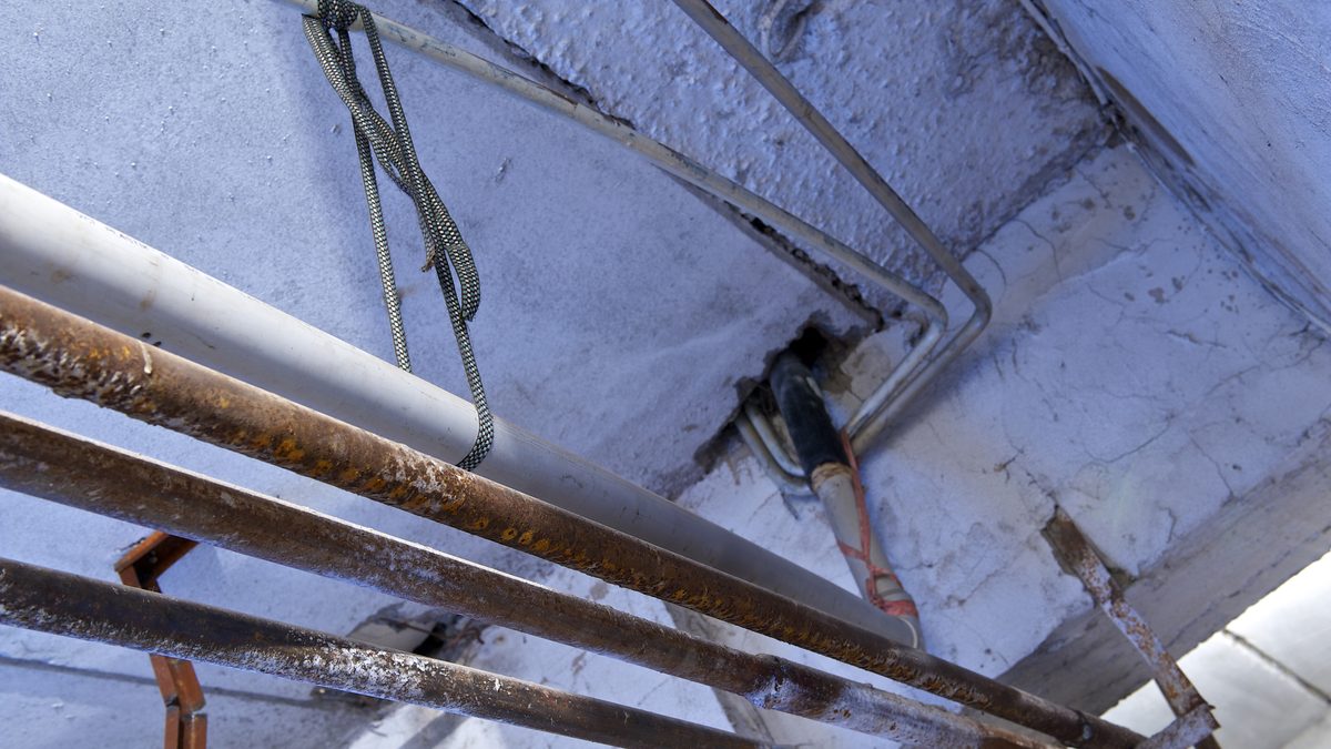 Rusted steel pipes and a plastic run along a basement ceiling